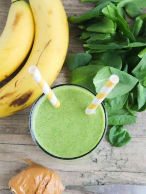 green breakfast smoothie in glass with two paper straws and banana with peanut butter