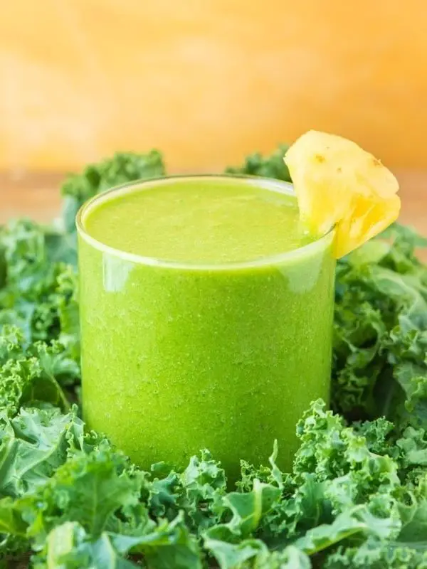 kale pineapple green smoothie in short glass with fresh kale and pineapple wedge
