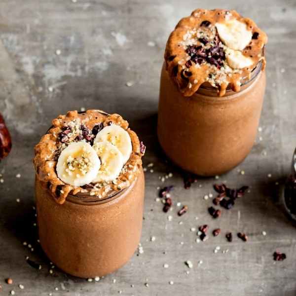 two chocolate banana protein shakes in glass jars with sliced banana topping