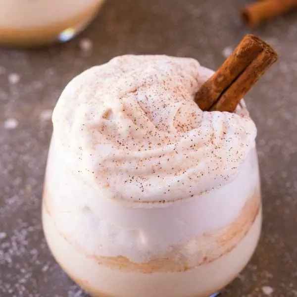 cinnamon roll breakfast protein shake in glass with whipped cream and cinnamon stick